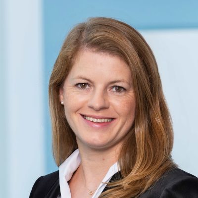 Portrait von Anne-Kathrin Roth im Businessanzug vor hellblauem Huntergrund