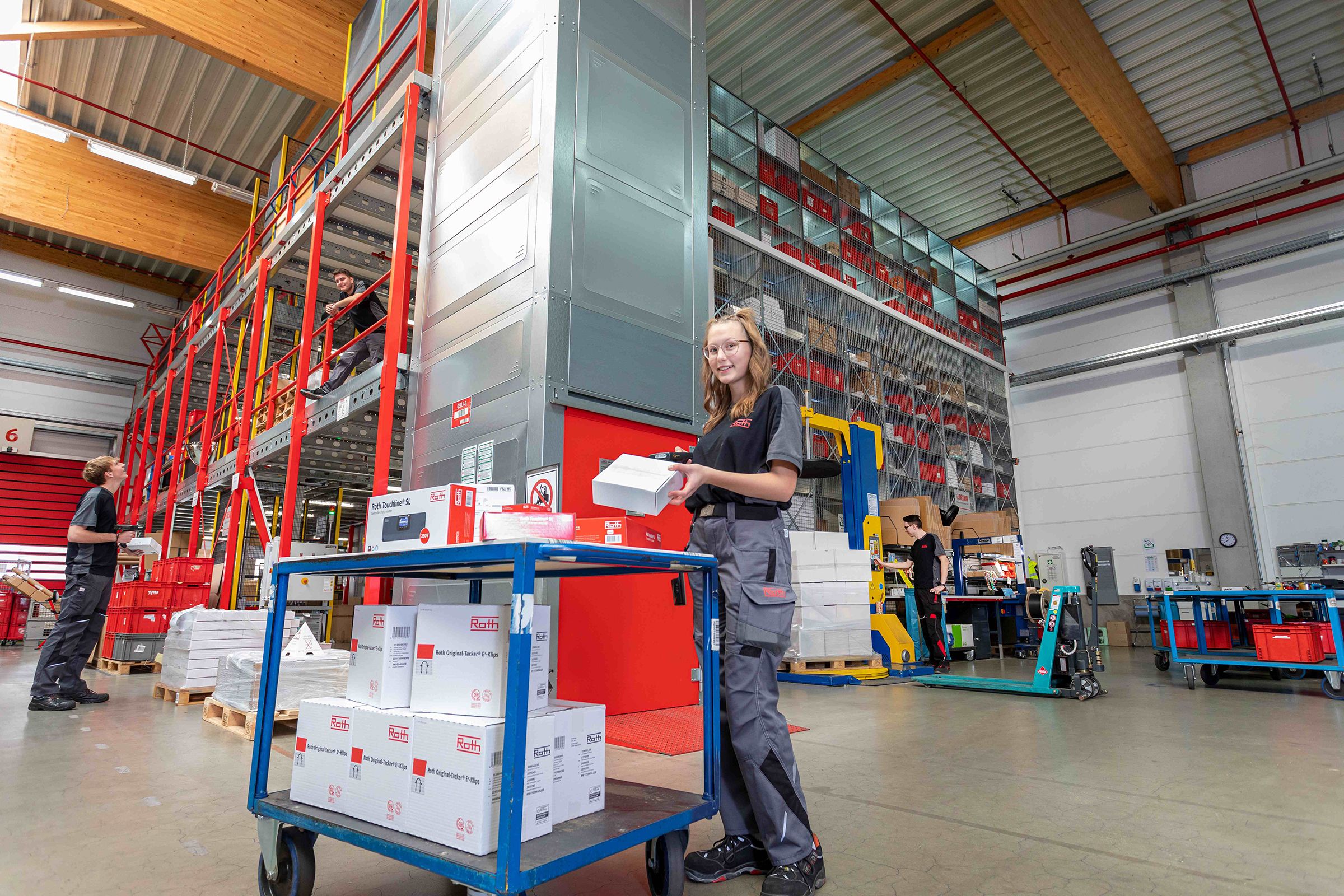 Junge Auszubildende in einer Industriehalle beim Scannen von Kartons