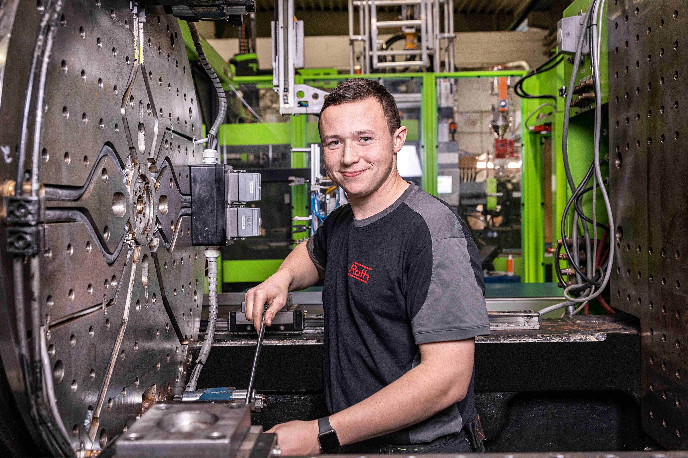 Junger Auszubildender an einer großen Industriemaschine mit einem Werkzeug in der Hand