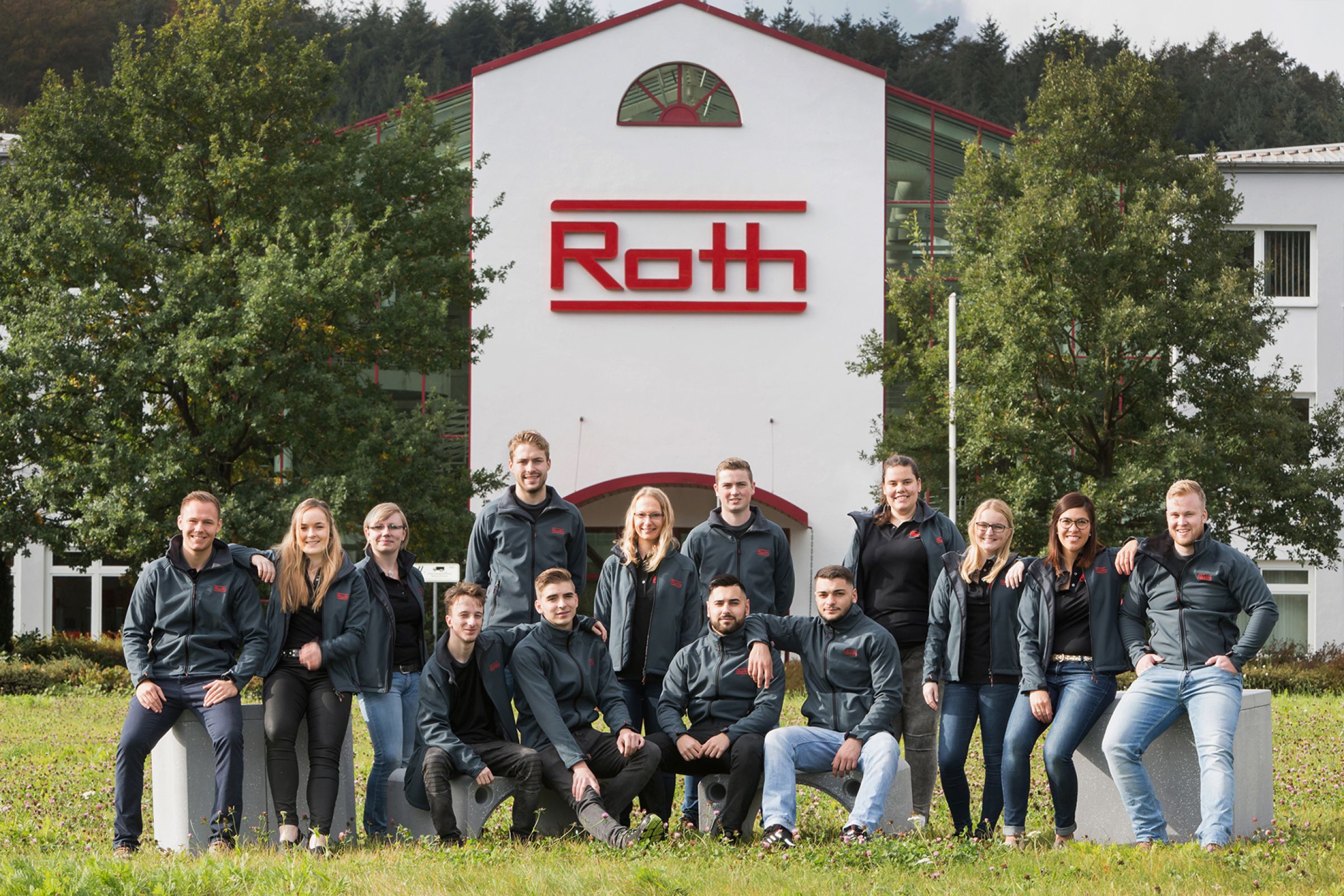14 Auszubildende von Roth Industries auf einer Wiese vor dem Firmengebäude.