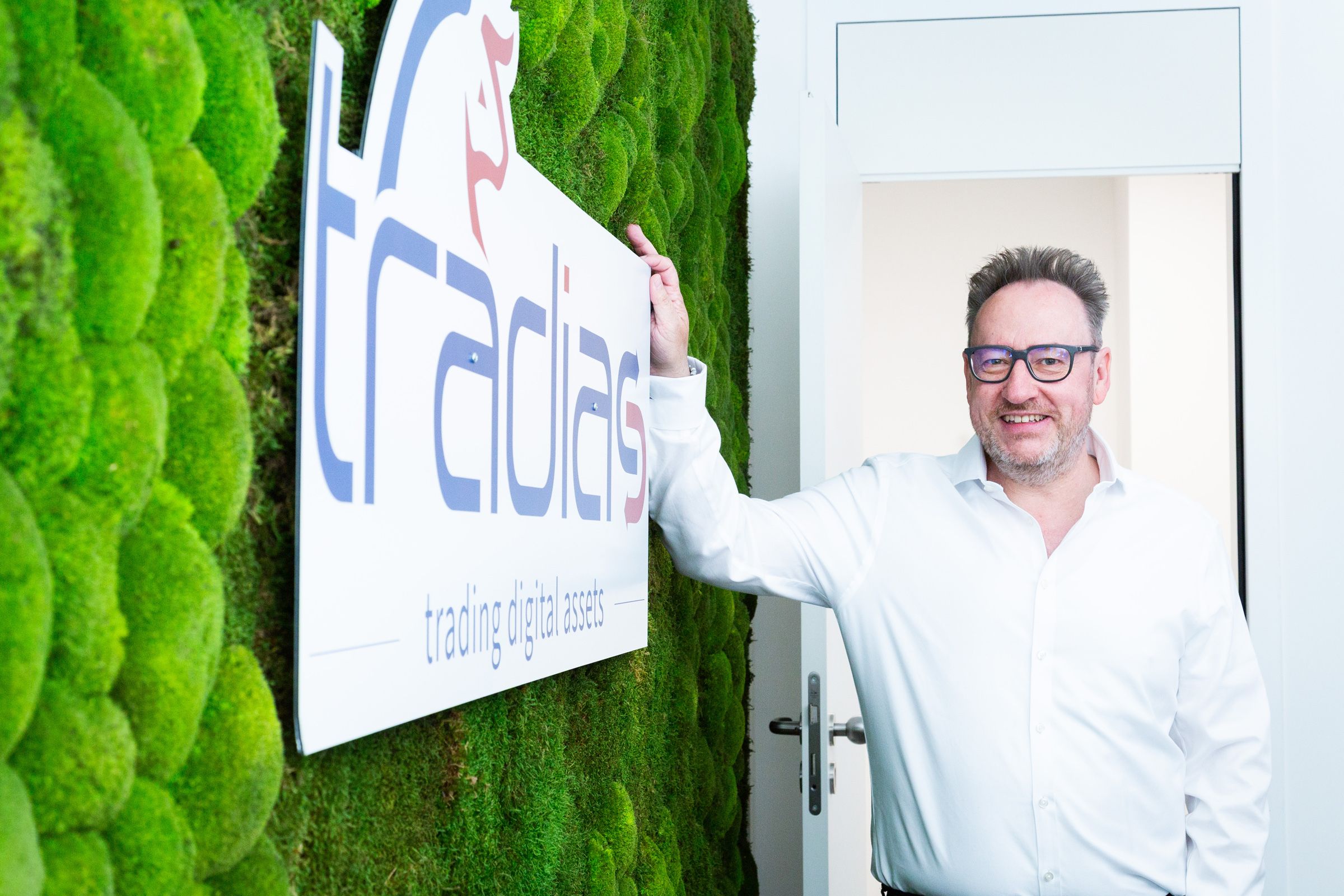 Michael Reinhard, CEO von Tradias steht angelehnt an eine Wand, an der linken  Wand ist das Logo tradias zu sehen.