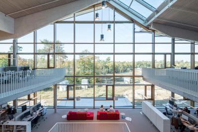 Blick in den Alnatura Campus in Darmstadt mit einigen Arbeitsplätzen und Ausblick aus dem Gebäude durch eine Glasfront ins Grüne.